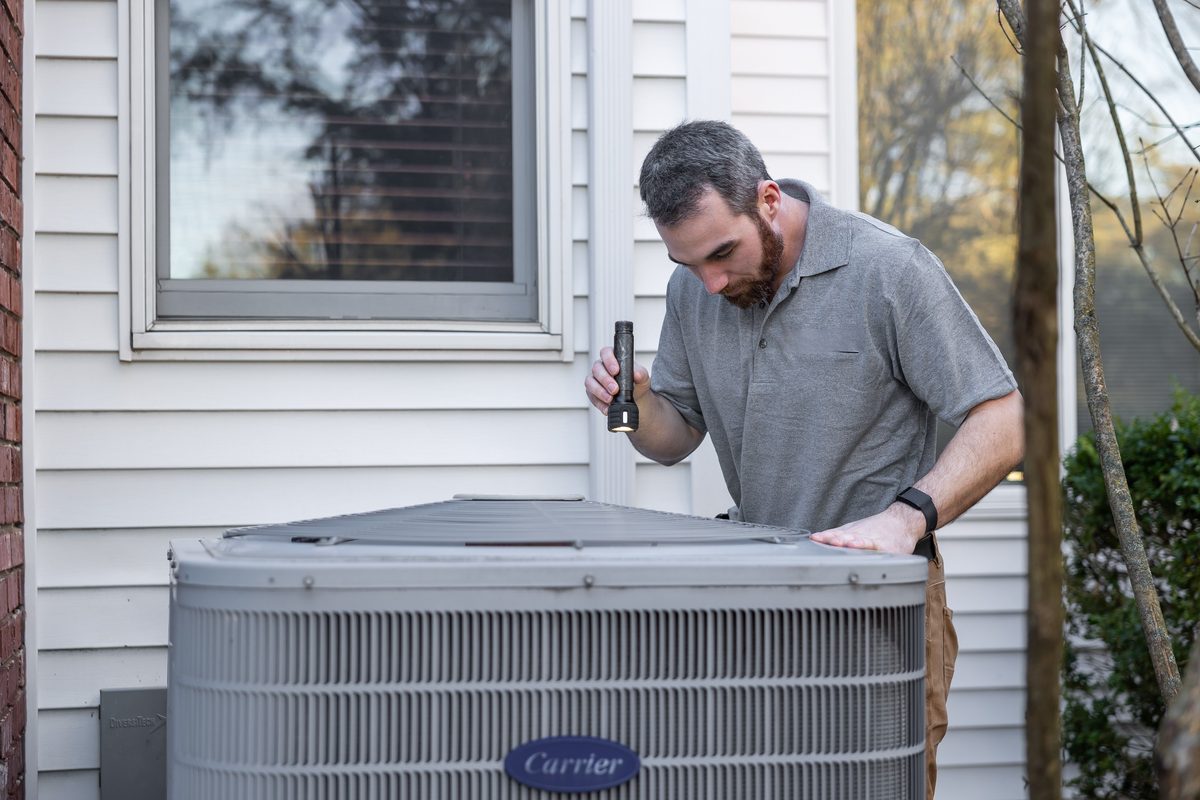 HVAC technician performing a seasonal maintenance tune-up on an outdoor air conditioning unit at a Dallas home